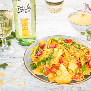 Ein ansprechendes Gericht mit Nachos, belegt mit Käse und frischen Zutaten, neben einem Glas sprudelndem Wein präsentiert.