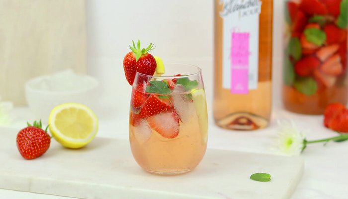 Ein erfrischendes Getränk mit frischen Erdbeeren und Minze, serviert in einem Glas mit Eiswürfeln und einer Zitronenscheibe.