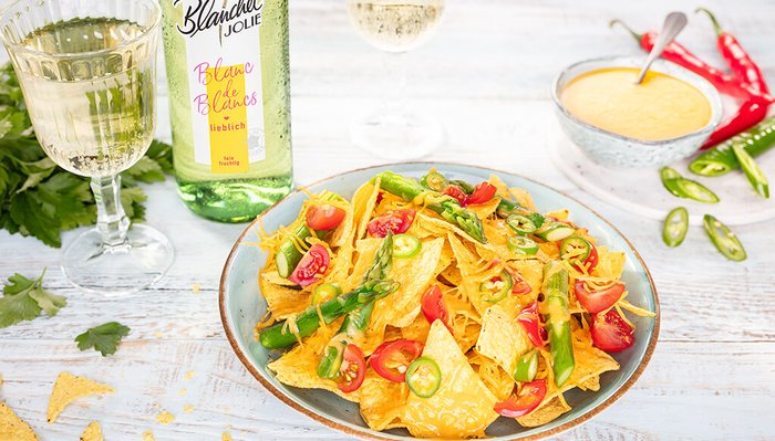Ein Teller mit knusprigen Nachos, belegt mit geschmolzenem Käse, frischen Tomaten und grünen Bohnen, umgeben von frischen Zutaten.