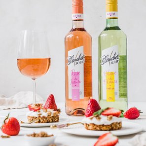 Zwei Flaschen Wein von Blanchet stehen neben einem Glas Rosé, während frische Erdbeeren und Desserts auf dem Tisch arrangiert sind.