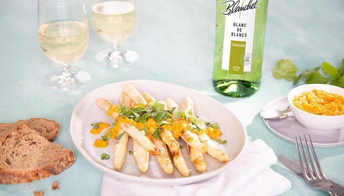 Ein Teller mit gebratenem Spargel, garniert mit frischem Koriander und einer fruchtigen Sauce, serviert mit Brot.