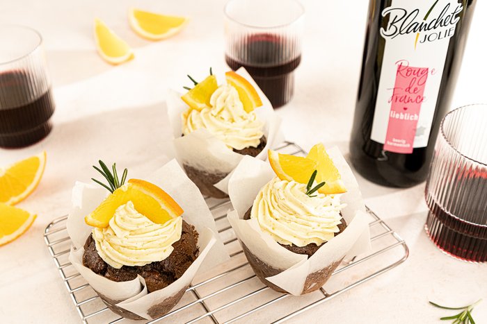 Drei köstliche Schokoladenmuffins mit Sahnehaube und Orangenscheiben, umgeben von frischen Zitronenscheiben und Rotwein.