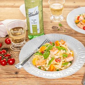 Ein stilvoll angerichteter Teller mit Pasta, Lachs und Gemüse, umgeben von einem rustikalen Ambiente und einem Glas Wein.