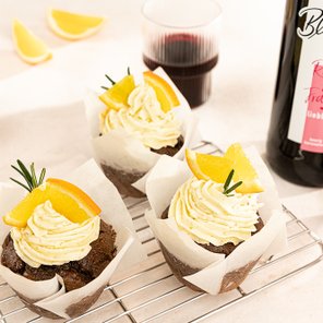 Drei köstliche Schokoladenmuffins mit Sahnehaube und Orangenscheiben, umgeben von frischen Zitronenscheiben und Rotwein.