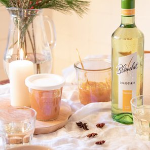 Ein rustikaler Tisch mit einem Glas Chardonnay von Blanchet, einer Kerze und verschiedenen Gläsern, die eine gemütliche Atmosphäre schaffen.