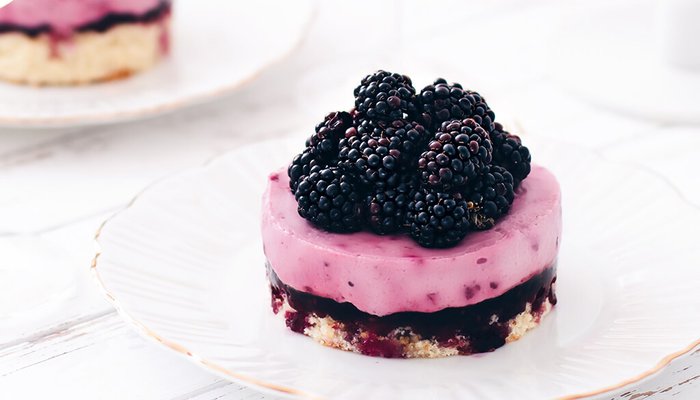 Ein köstlicher, mehrschichtiger Kuchen mit einer cremigen, lila Schicht und frischen Brombeeren obendrauf auf einem weißen Teller.