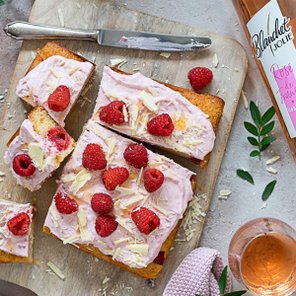 Ein köstlicher, in Stücke geschnittener Kuchen mit rosa Sahne, frischen Himbeeren und weißen Schokoladenstückchen auf einem Holzbrett.