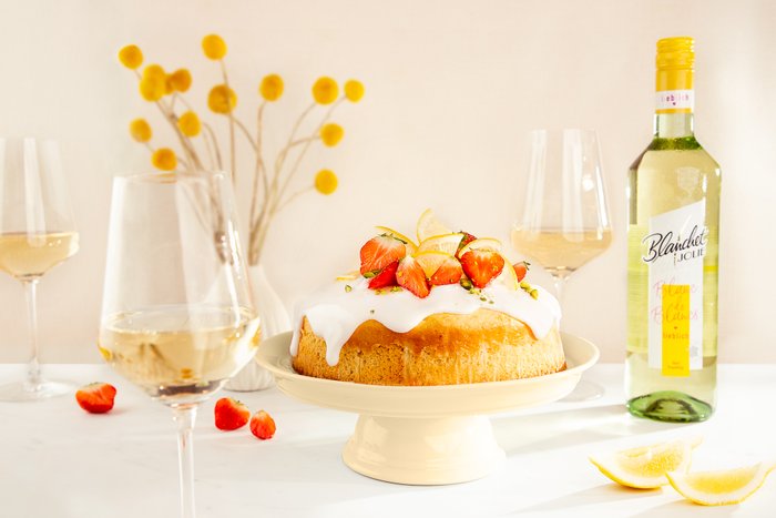 Ein köstlicher Kuchen mit einer weißen Glasur, garniert mit frischen Erdbeeren und Zitronenscheiben, steht auf einem eleganten Teller.