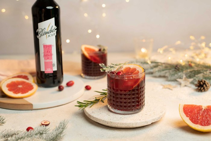 Ein elegantes Glas mit einem fruchtigen Getränk, garniert mit Grapefruit und Preiselbeeren, steht auf einem hellen Tisch.