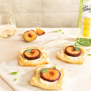 Drei köstliche Obsttörtchen mit Pflaumen und Minze auf einem Marmorbrett, umgeben von frischen Pflaumenstücken.