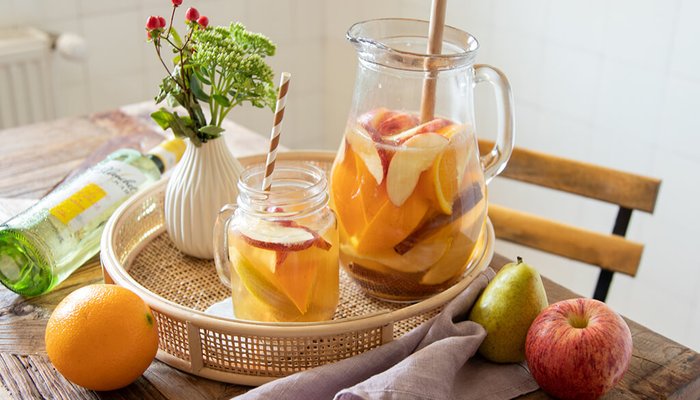 Ein rustikaler Tisch mit einer Karaffe gefüllt mit fruchtigem Getränk, umgeben von frischen Früchten und einer kleinen Vase.