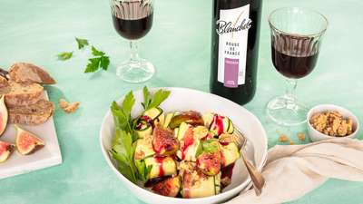 Ein elegantes Gericht aus Zucchini und Feigen, garniert mit Walnüssen und einem fruchtigen Sirup, serviert in einer weißen Schüssel.