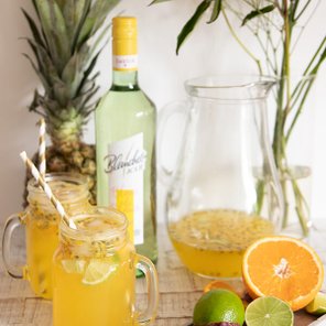 Zwei Gläser mit erfrischendem Getränk, umgeben von frischen Früchten und einer Flasche Blanquette auf einem Holztisch.