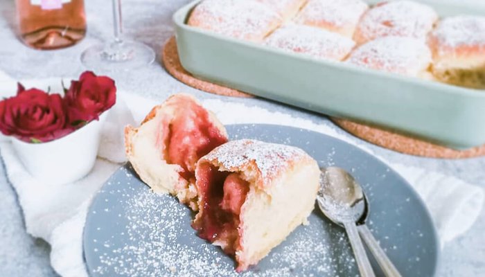 Ein Stück frisch gebackener Kuchen mit einer fruchtigen Füllung, bestäubt mit Puderzucker, auf einem grauen Teller.