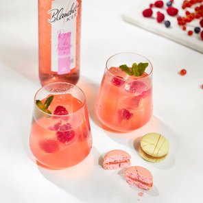 Zwei Gläser mit erfrischendem rosa Getränk, garniert mit frischen Himbeeren und Minze, stehen auf einem weißen Tisch.