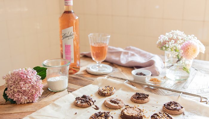 Ein rustikaler Holztisch mit frisch gebackenen Keksen, einer Flasche Roséwein von Blanchet und bunten Blumenarrangements im Hintergrund.