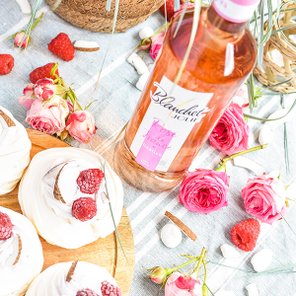 Eine rustikale Holzplatte mit köstlichen Desserts, dekoriert mit Himbeeren, umgeben von frischen Rosen und einer Flasche Roséwein.
