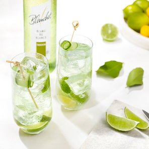 Eine Flasche Blanc de Blancs von Blanchet steht neben zwei Gläsern mit einem erfrischenden, limettengrünen Cocktail und Eiswürfeln.