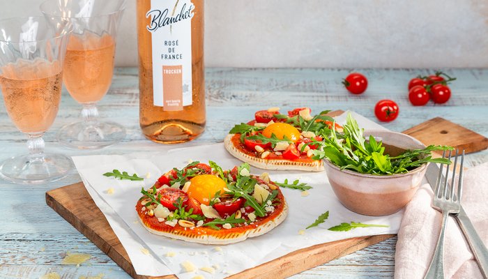 Zwei köstliche belegte Brote mit frischen Tomaten, Rucola und einem Spiegelei, umgeben von einem Glas Roséwein.