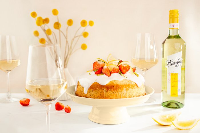 Ein köstlicher Kuchen mit einer weißen Glasur, garniert mit frischen Erdbeeren und Zitronenscheiben, steht auf einem eleganten Teller.