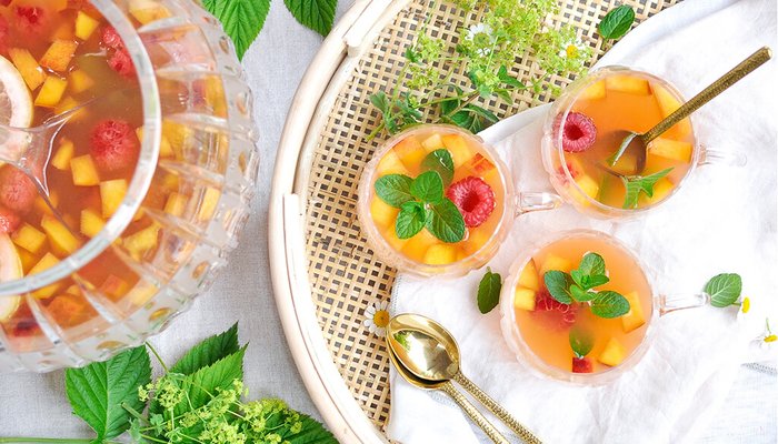 Eine elegante Glaskaraffe mit fruchtigem Getränk, gefüllt mit bunten Stückchen von Melone und Himbeeren, steht auf einem Tisch.