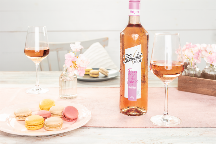 Ein eleganter Tisch mit einem Flasche Roséwein und Gläsern, umgeben von bunten Macarons und zarten Blumenarrangements.