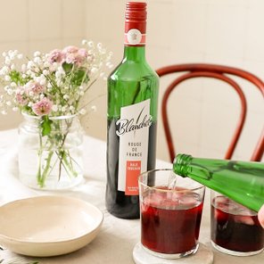 Eine Flasche Blanchet Rouge de France steht auf einem Tisch, während ein Glas mit rotem Getränk gefüllt wird.