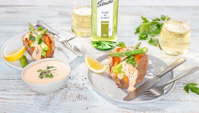 Ein ansprechendes Gericht mit gefüllten Süßkartoffeln, frischem Gemüse und Dip, serviert mit Zitrone und einem Glas trockenen Weißwein.