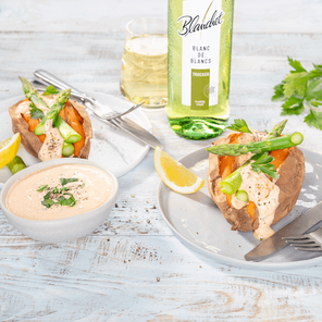 Leckere Süßkartoffeln mit Spargel und einer Sauce, serviert auf einem Holztablett mit einem Glas erfrischendem Weißwein.