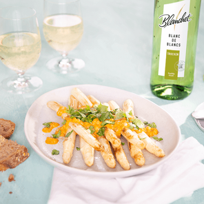 Ein Teller mit gebratenem Spargel, garniert mit frischem Koriander und einer fruchtigen Sauce, umgeben von Gläsern Weißwein.