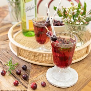 Zwei Gläser mit rotem Getränk, dekoriert mit Beeren und Strohhalmen, stehen auf einem Tablett aus Rattan.