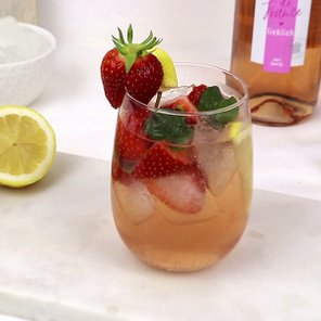Ein erfrischendes Getränk in einem Glas, gefüllt mit Eis, Erdbeeren und Minze, neben einer halben Zitrone auf einem Tisch.