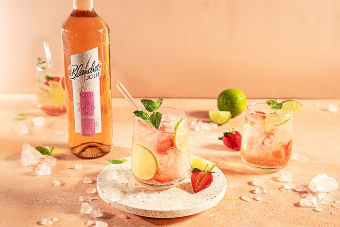 Ein erfrischendes Getränk mit Limetten- und Erdbeerstücken, garniert mit frischer Minze, auf einem hellen Untergrund.