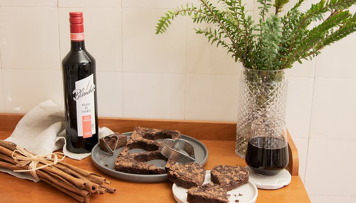 Ein Flasche Rotwein steht neben einem Teller mit herzförmigen Schokoladenkeksen auf einem Holztisch.