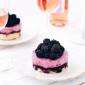 Ein köstlicher, runder Kuchen mit einer Schicht aus Himbeermousse und einer Füllung aus Brombeeren auf einem eleganten Teller.