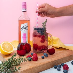 Ein Glas mit einem fruchtigen Getränk, gefüllt mit Himbeeren, Heidelbeeren und einem Strohhalm, steht auf einem Holzbrett.