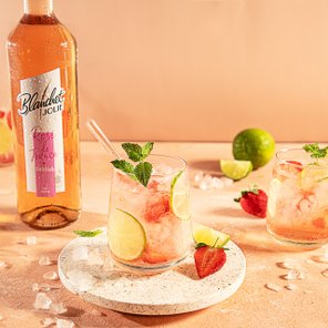 Ein erfrischendes Getränk mit Limetten- und Erdbeerstücken, garniert mit frischer Minze, auf einem hellen Untergrund.