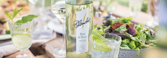 Ein eleganter Tisch mit einem Flasche Blanc de Blancs, frischen Salat und Gläsern, die auf eine gesellige Mahlzeit hinweisen.