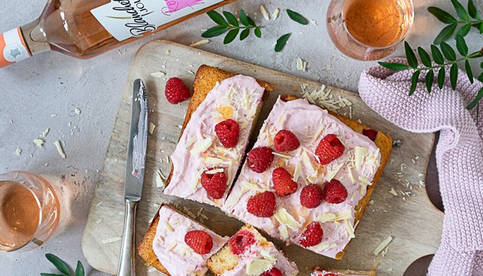 Ein köstlicher Kuchen mit einer rosa Creme, garniert mit frischen Himbeeren und weißen Schokoladenstückchen auf einem Holzbrett.