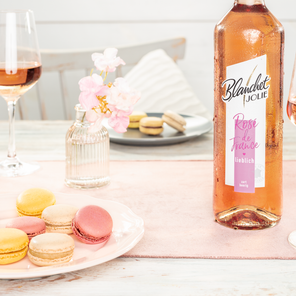 Ein eleganter Tisch mit einem Roséwein, Gläsern und bunten Macarons, umgeben von zarten Blumen in einer Glasvase.
