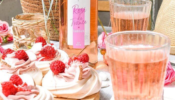 Ein rustikaler Tisch mit köstlichen Baisers, die mit Himbeeren und Sahne dekoriert sind, umgeben von frischen Blumen.