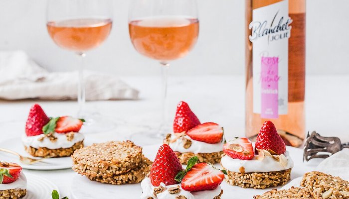 Zwei Gläser Roséwein stehen neben einer Auswahl an köstlichen Desserts mit Erdbeeren und Joghurt auf einem weißen Tisch.