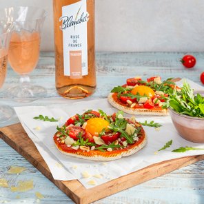 Zwei knusprige Tartes mit frischen Tomaten, Rucola und einem Eigelb, serviert auf einem Holzbrett.