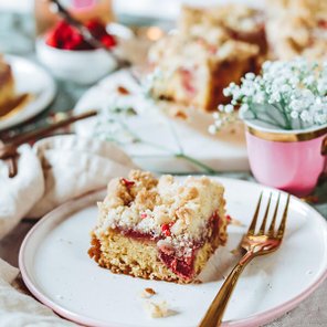 Ein Stück fruchtiger Kuchen mit einer knusprigen Streuselschicht, serviert auf einem weißen Teller mit goldener Gabel.