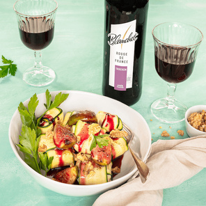 Ein köstlicher Salat aus Zucchini und Feigen, verfeinert mit Walnüssen, begleitet von einem Glas Rotwein auf einem hellen Tisch.