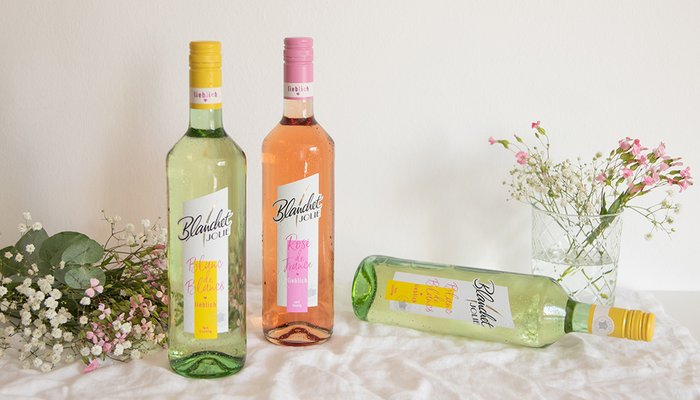 Drei Flaschen Wein von Blanchet stehen auf einem Tisch, umgeben von zarten Blumen und einem frischen, hellen Hintergrund.