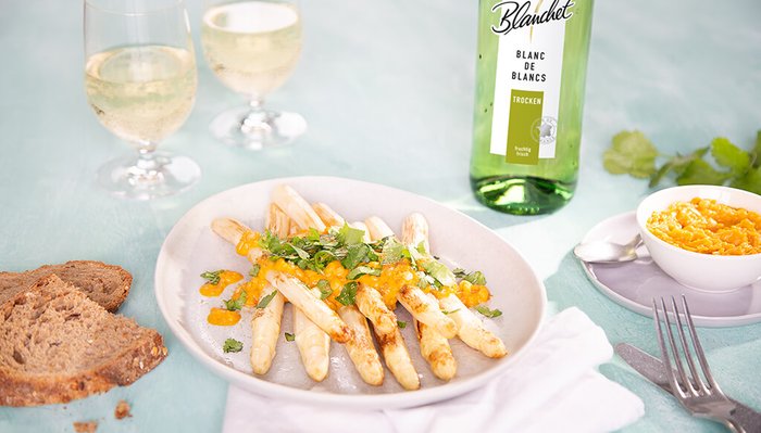 Ein Teller mit gebratenem Spargel, garniert mit frischem Koriander und einer fruchtigen Sauce, serviert mit Brot.