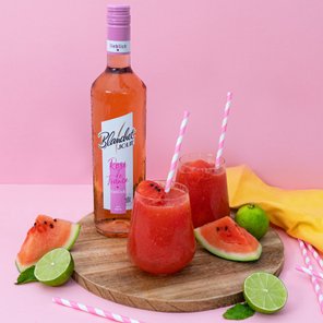 Zwei Gläser mit fruchtigem Getränk aus Wassermelone und Limette stehen auf einem Holzbrett, umgeben von frischen Früchten.