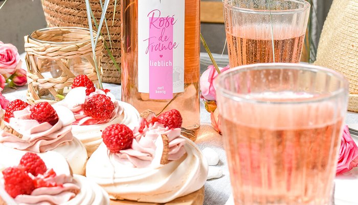 Ein rustikaler Tisch mit köstlichen Baisers, die mit Himbeeren und Sahne dekoriert sind, umgeben von frischen Blumen.
