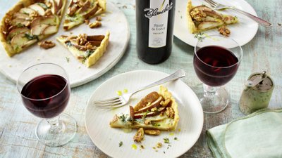 Ein köstlicher Apfelkuchen mit Walnüssen, serviert mit einem Glas Rotwein auf einem rustikalen Tisch.